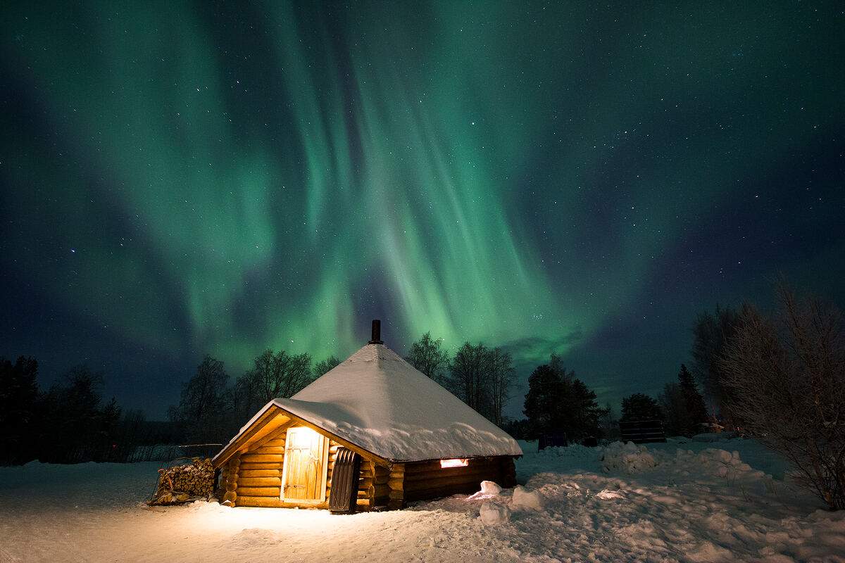 Aurora boreal sobre una cabaña de madera en Laponia, expedición fotográfica de Ecotour