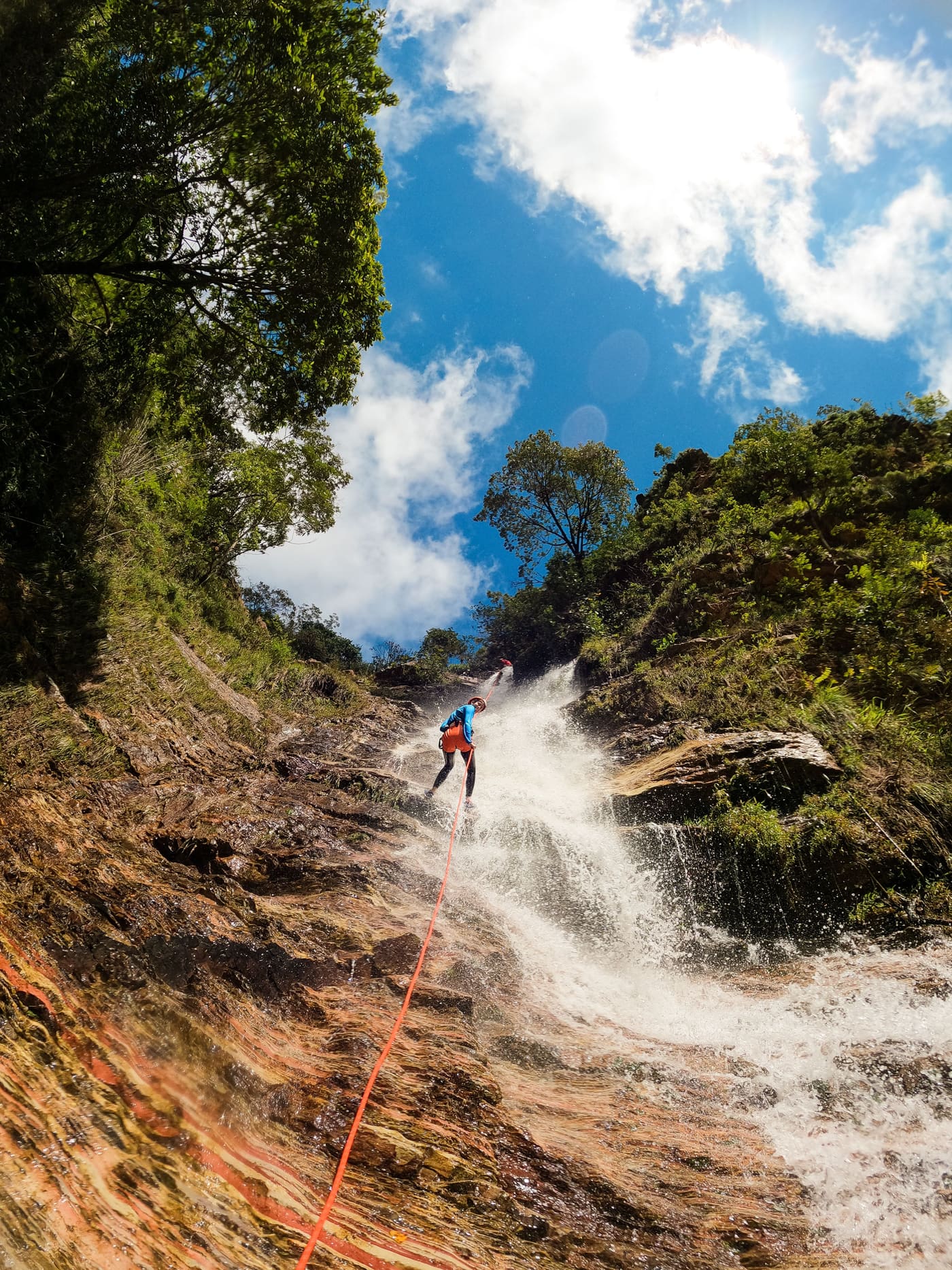 Descenso de barranco en día soleado, con tobogán de agua entre vegetación