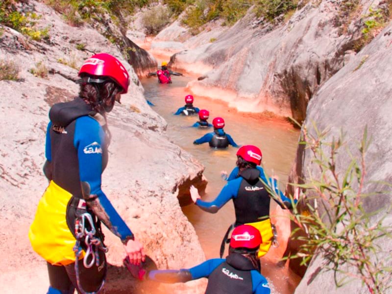 Grupo con casco y neopreno avanzando por un cañón estrecho de roca con pozas, en un barranco del Pirineo