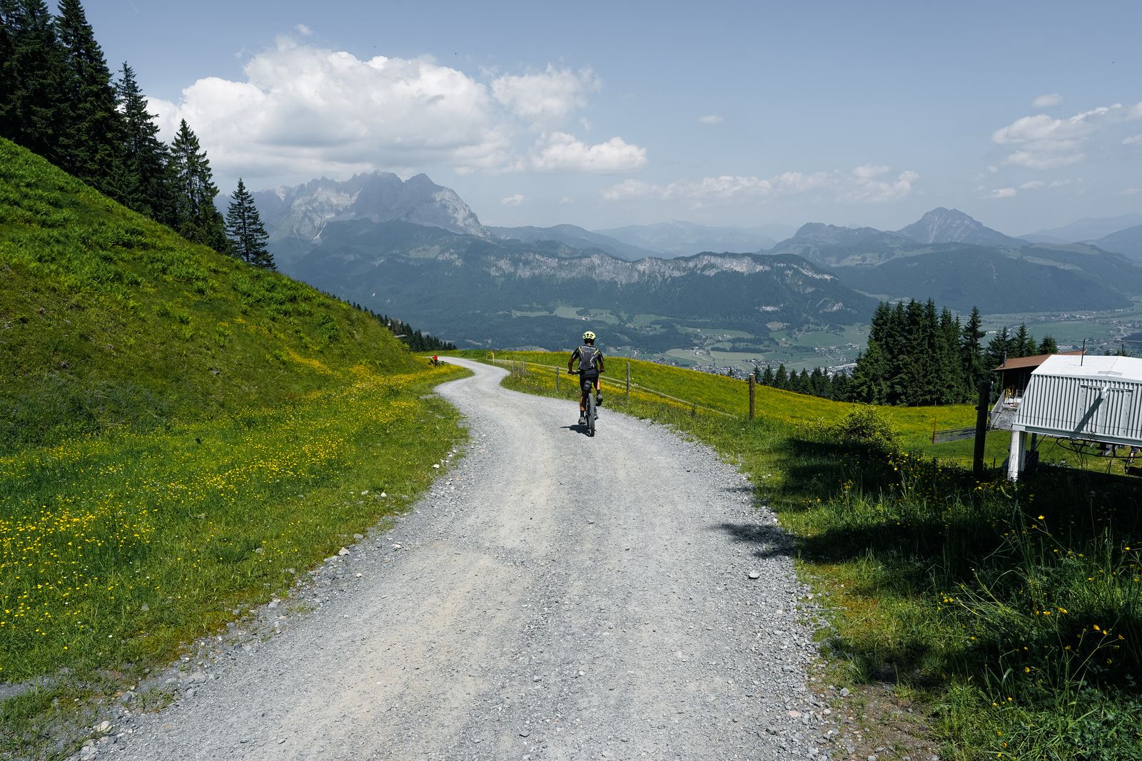 Ciclista en e-bike por un camino de grava de alta montaña, con valle alpino y picos al fondo