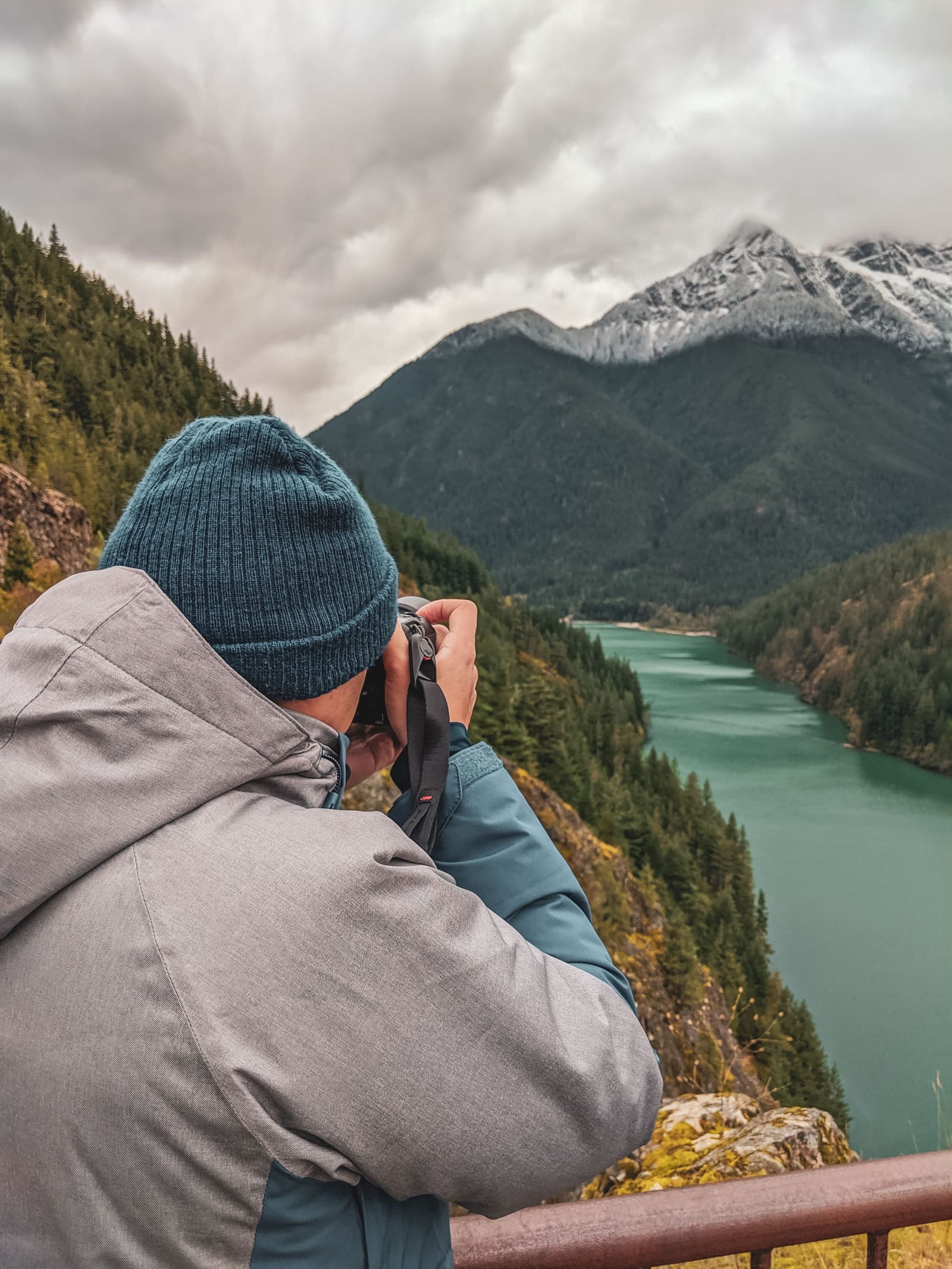 Fotógrafo con cámara junto a un lago de montaña, con picos nevados al fondo