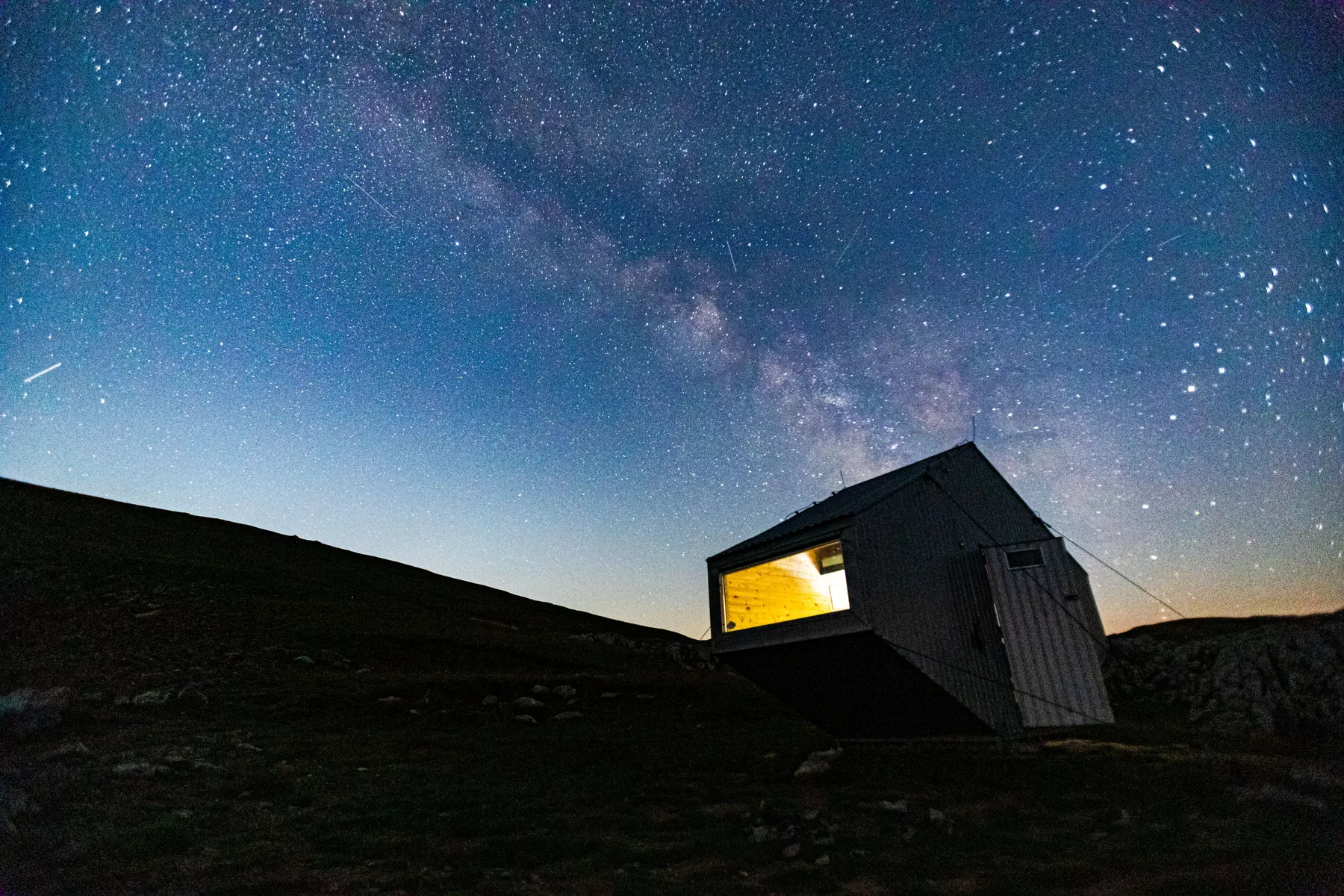 Refugio de montaña iluminado de noche bajo un cielo estrellado con la Vía Láctea
