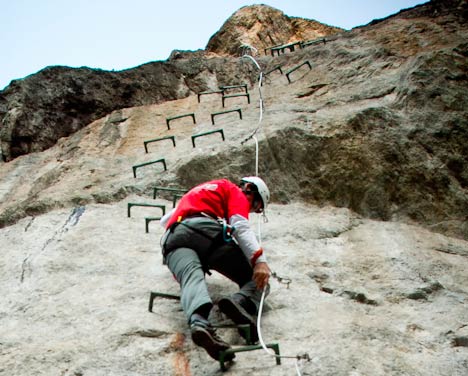 Persona ascendiendo una via ferrata equipada con clavijas de acero sobre una pared de roca