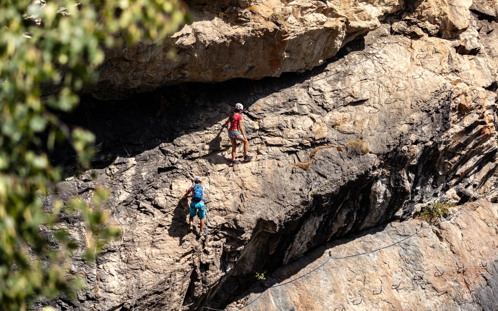 Dos personas progresando por una vía ferrata equipadas con casco y arnés