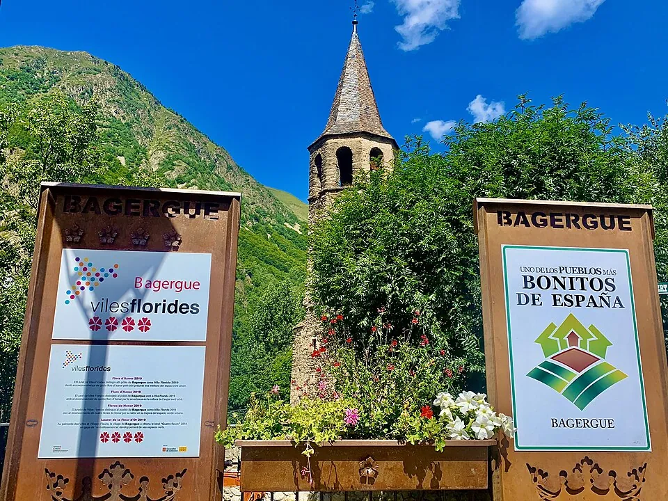 Campanario de Bagergue tras los carteles de Pueblos Más Bonitos de España y Viles Florides