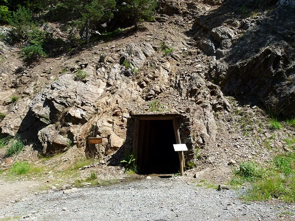 Boca de una galería de la Mina Victòria entre rocas, con cartel informativo