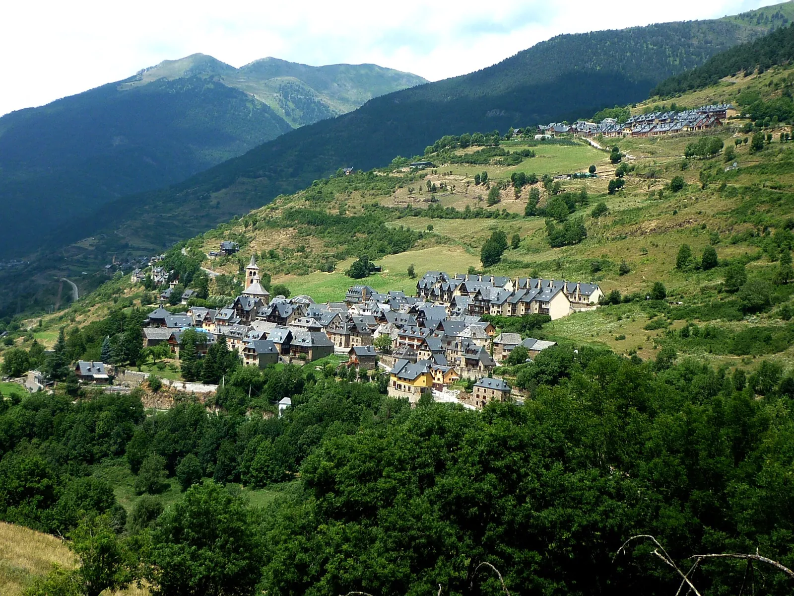 Vilac y su ladera verde vistos desde lejos, con el valle y las montañas detrás