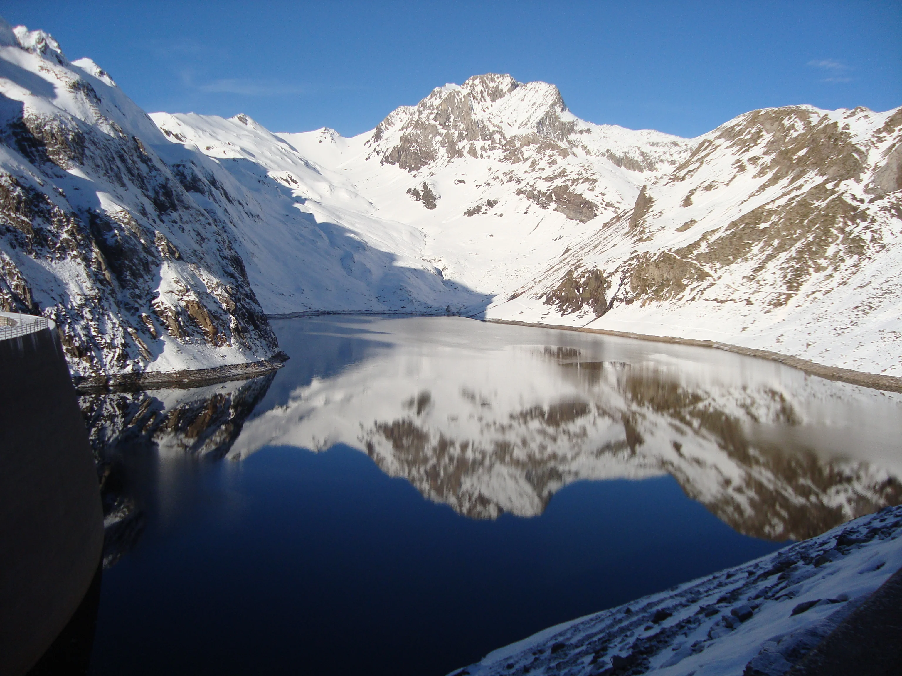 Presa del embalse de Llauset en invierno, con el agua helada reflejando las montañas