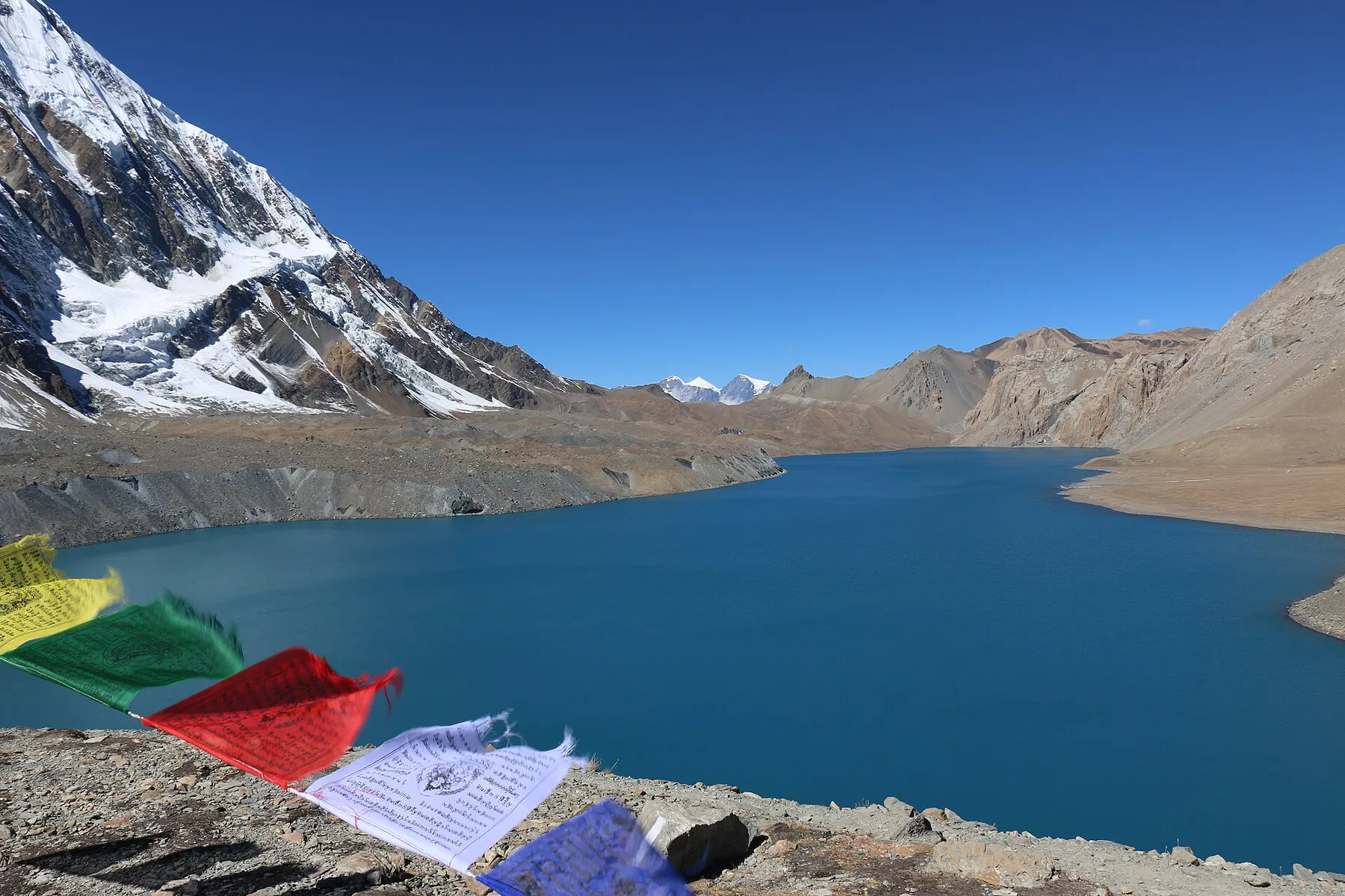 El lago Tilicho, de agua turquesa, bajo la montaña nevada, con banderas de oración en primer plano