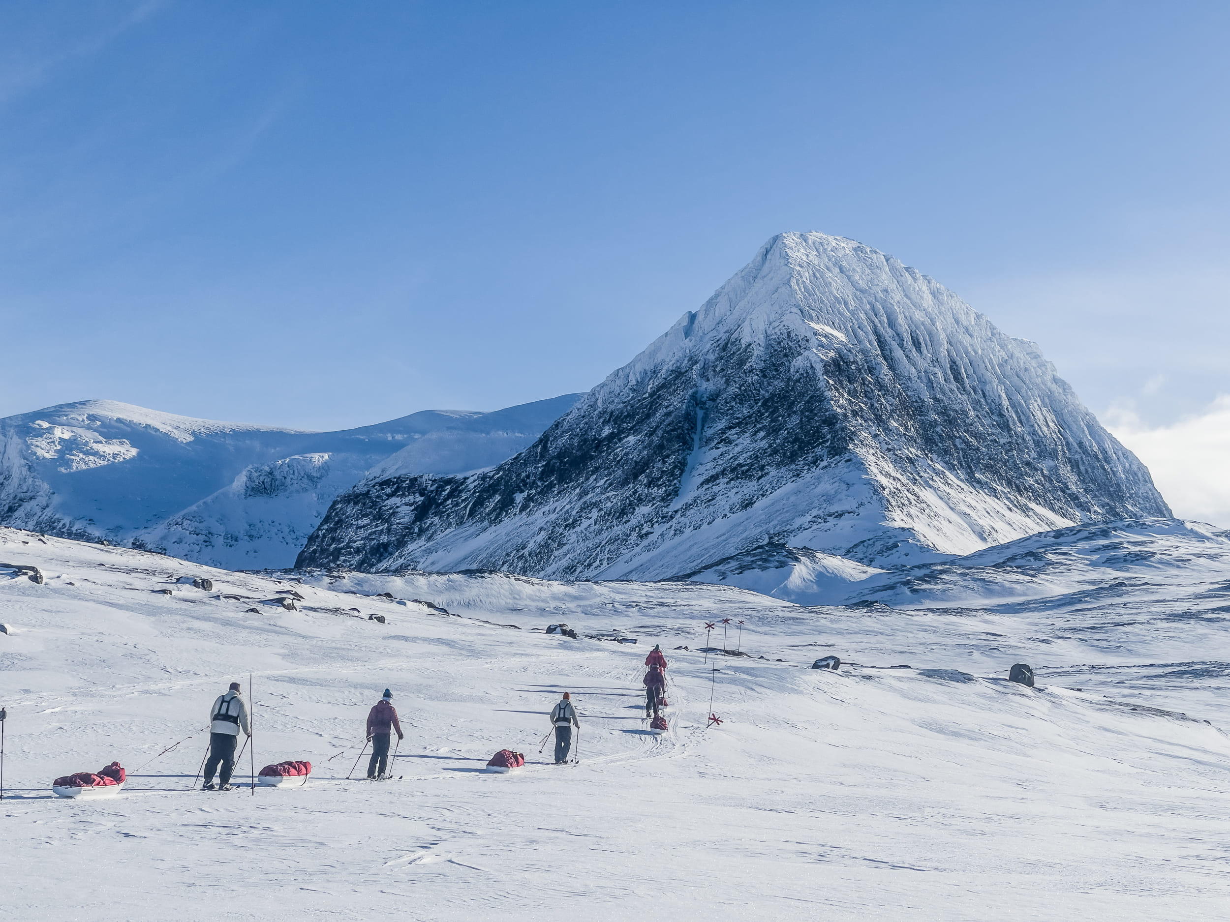 Grupo esquiando con pulka por un valle nevado en la Laponia sueca
