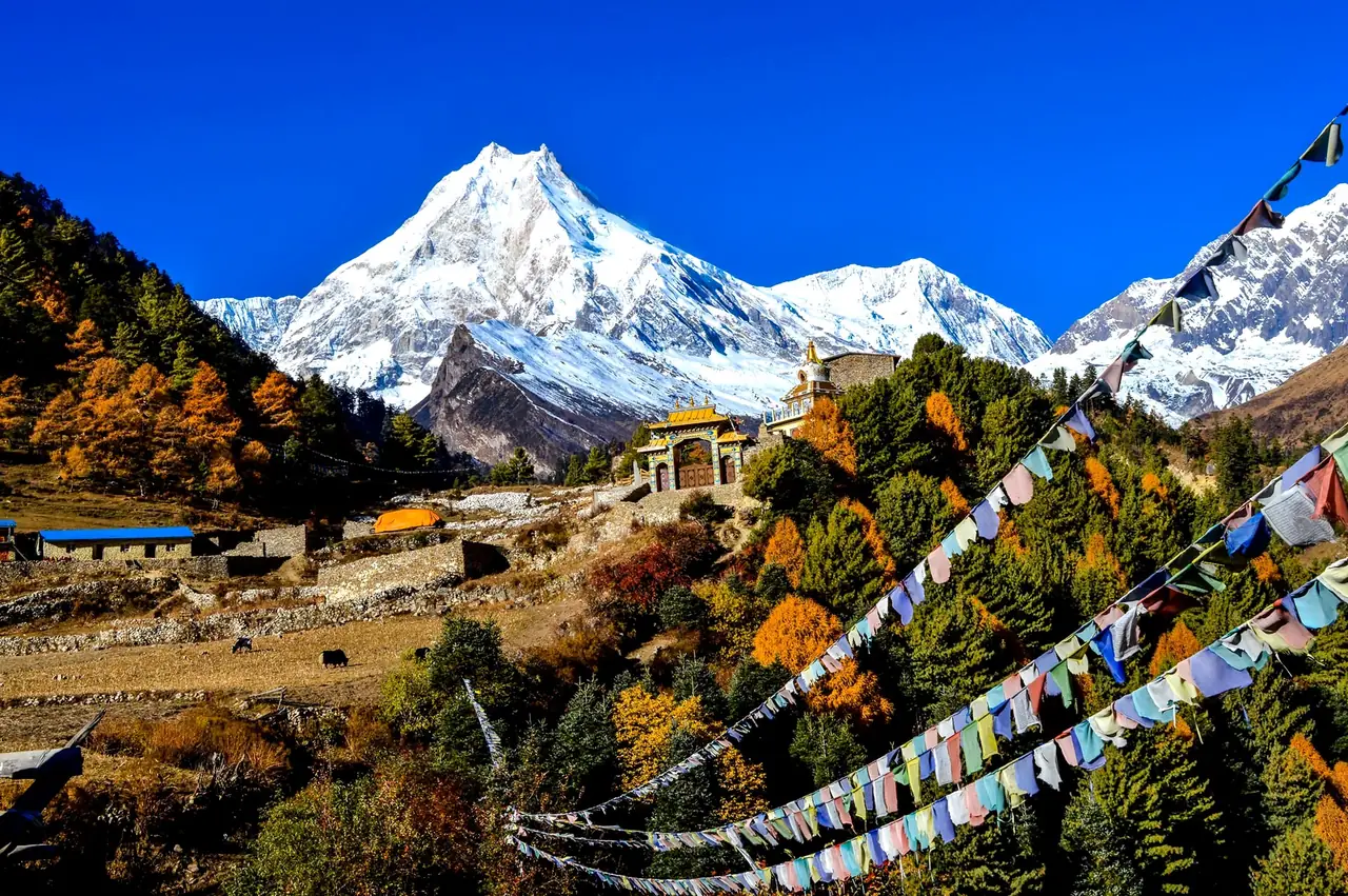 Banderas de oración budistas y monasterio con el Manaslu nevado al fondo, en otoño