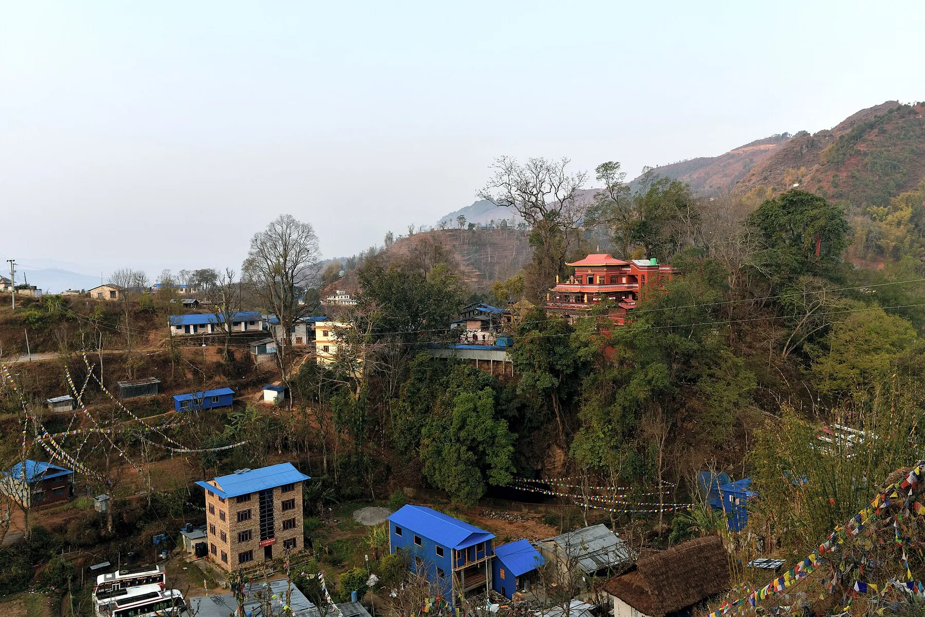 Aldea en la ladera de una colina de Khotang, con casas, bosque y banderas de oración