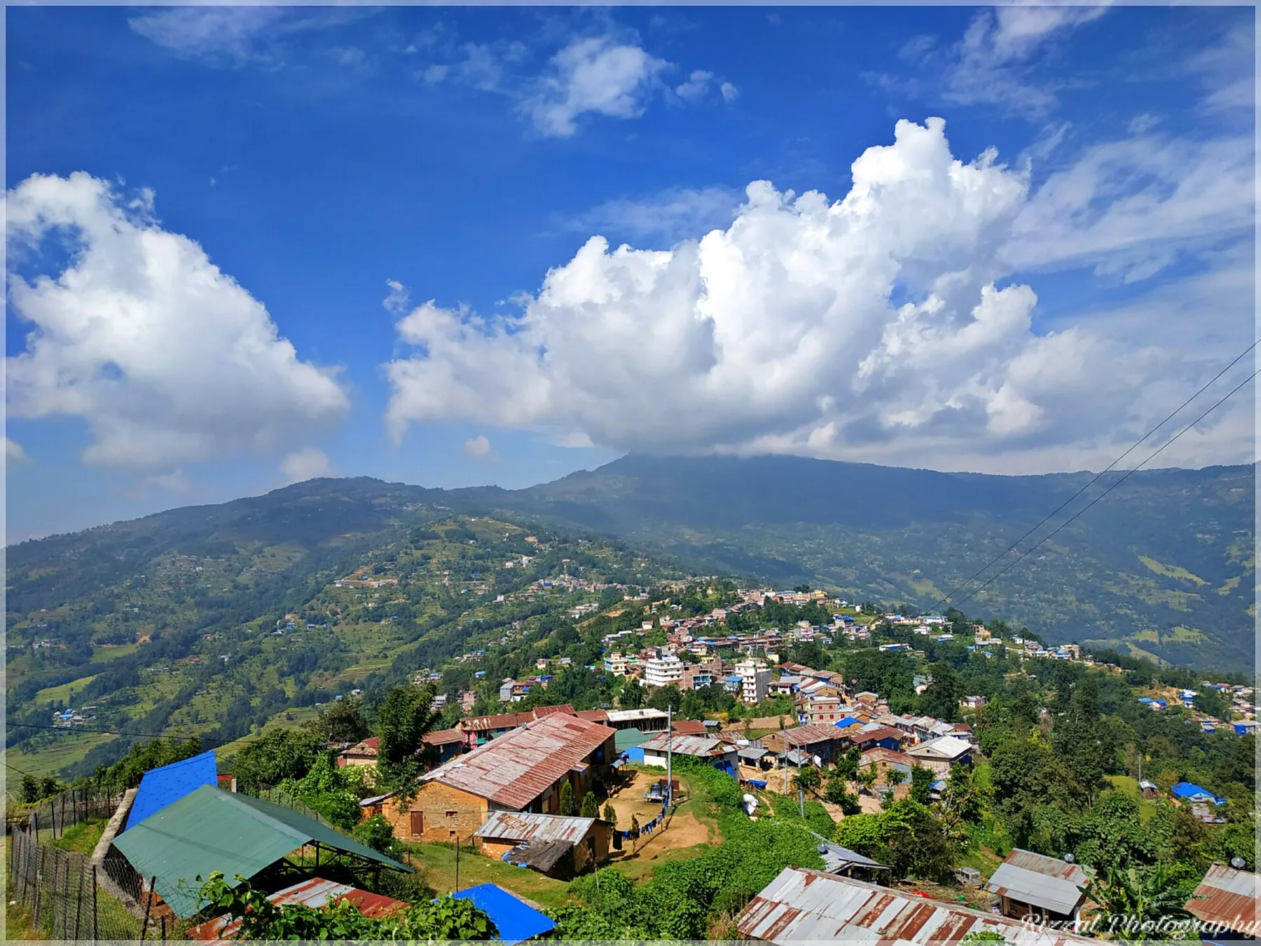 Aldea de colinas en el este de Nepal con casas de tejado de chapa, campos verdes y nubes de monzón