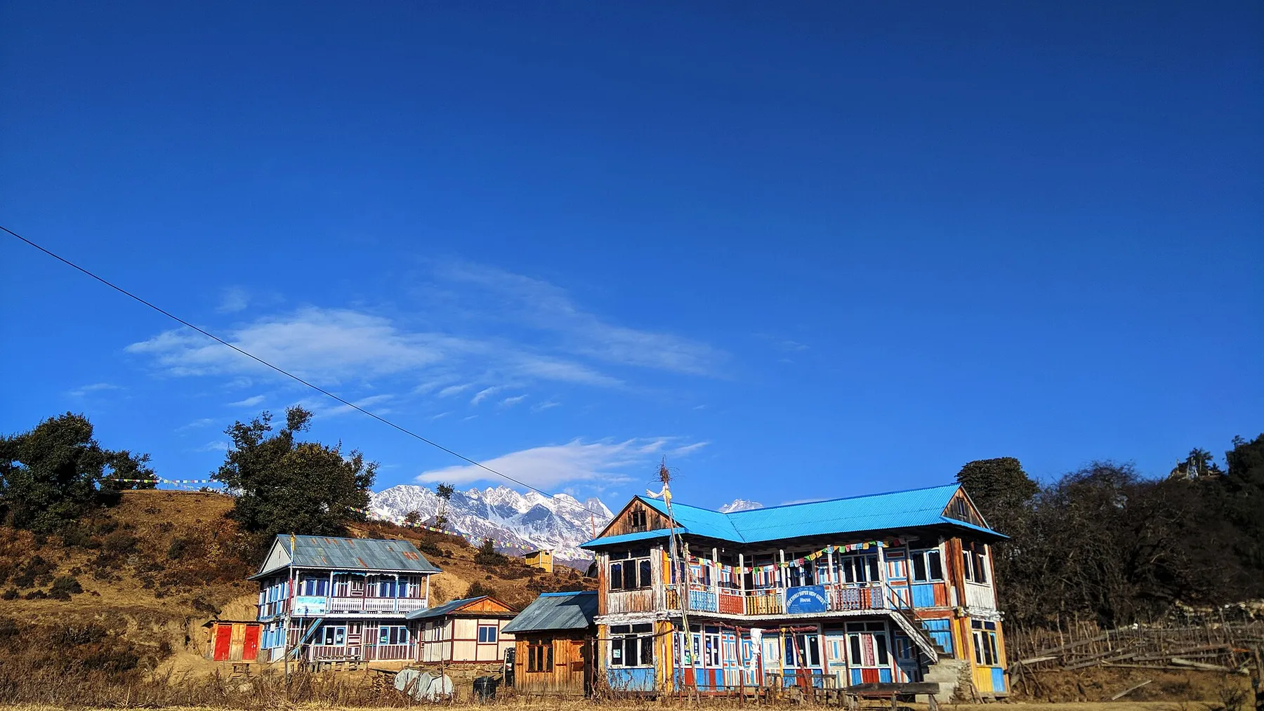 Lodge de colores en Nagthali, con la cordillera nevada del Himalaya al fondo y cielo azul